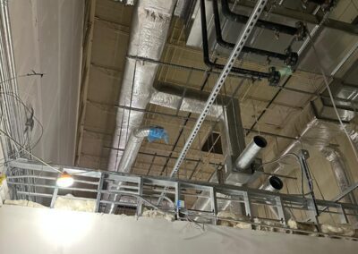 Exposed ceiling with insulated pipes, ductwork, and electrical conduits in an industrial setting.