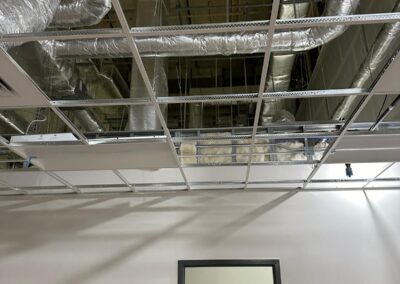 Industrial ceiling with insulated pipes and ductwork above a door in a room.