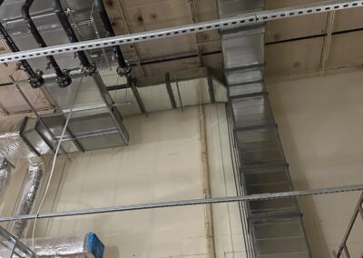 Interior view of industrial ceiling with ductwork, piping, and metal supports.
