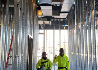 Two workers in high-visibility jackets inside a metal-studded construction site.
